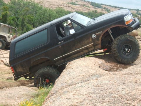 1995 Ford Bronco - A black 1995 Ford Bronco navigates a rocky terrain, with another vehicle visible behind it.