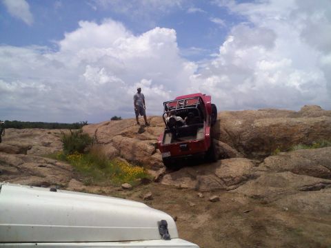 1995 Ford Bronco - Two off-road vehicles navigate a rocky terrain under a cloudy sky.