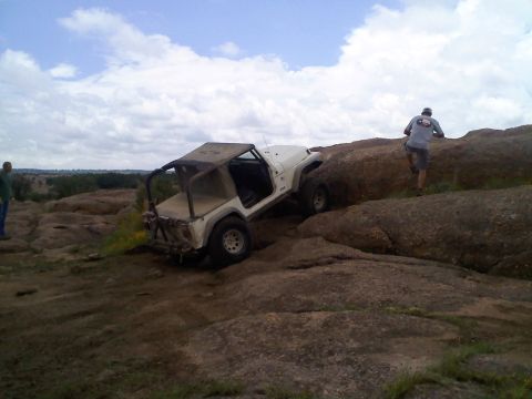 1995 Ford Bronco - A white Jeep navigates a challenging rocky trail under a cloudy sky.