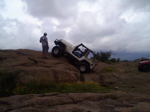 1995 Ford Bronco - A white Jeep Wrangler navigates a steep, rocky incline while another vehicle waits in the background under a cloudy sky.