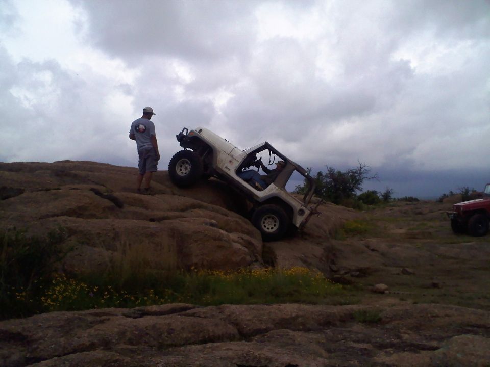 White Jeep Wrangler climbing rocky hill, another vehicle visible
