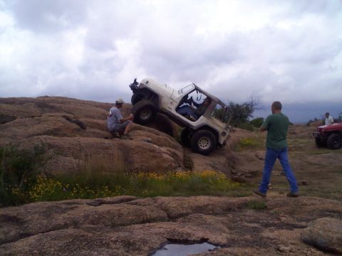 1995 Ford Bronco - White Jeep Wrangler navigating a challenging rocky terrain with assistance from observers.
