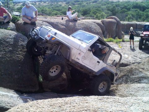 1995 Ford Bronco - A white Jeep Wrangler navigates a challenging rocky terrain with spectators observing the background.