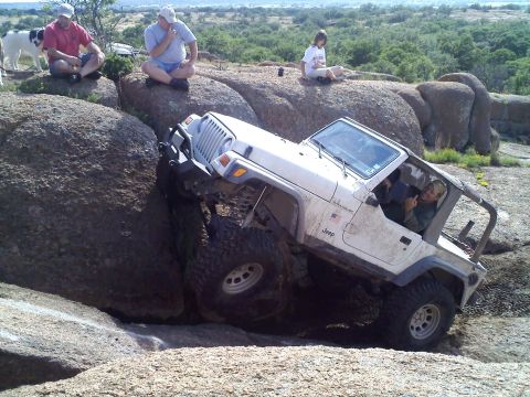 1995 Ford Bronco - A white Jeep Wrangler navigates a challenging rocky terrain with people watching.