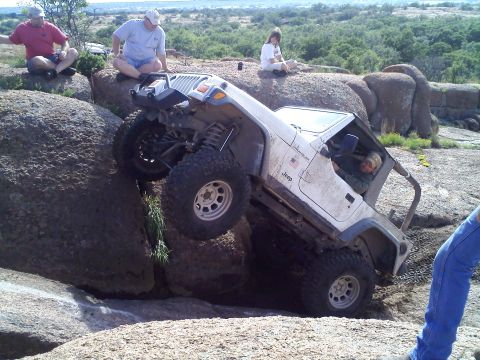 1995 Ford Bronco - A white Jeep Wrangler navigates a challenging rocky terrain, with spectators observing from above.