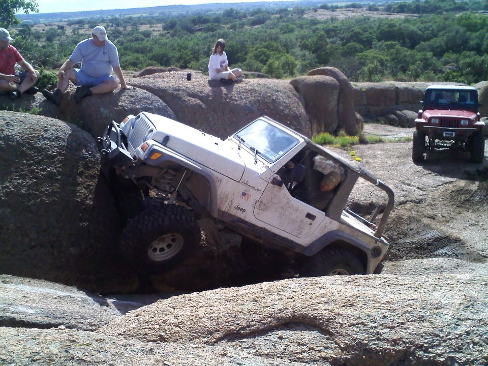 White Jeep Wrangler climbing over rocks with a red Jeep in the background