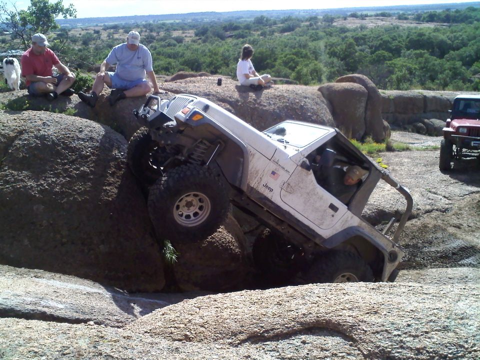 White Jeep Wrangler climbing over large rocks with people watching