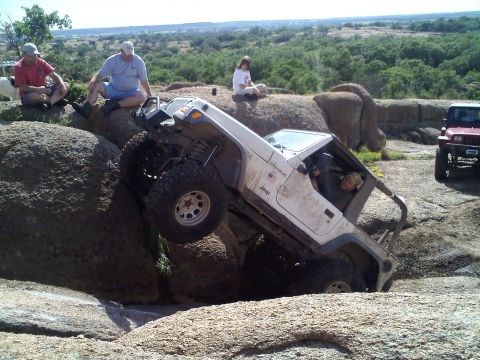 1995 Ford Bronco - A white Jeep Wrangler navigates a rocky terrain with spectators watching.