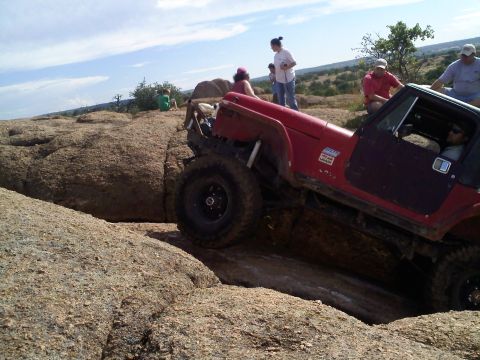 1995 Ford Bronco - Off-road Jeep navigates a rocky obstacle course under a partly cloudy sky.