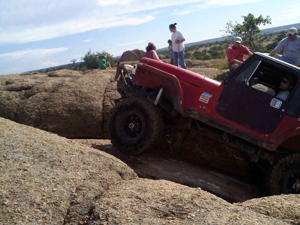 Red Jeep Wrangler climbing over large rocks on an off-road trail with people watching