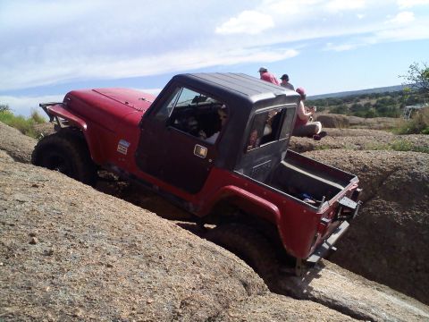 1995 Ford Bronco - A red Jeep navigates a rocky trail with passengers watching from the side.