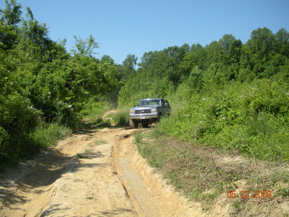 Silver lifted SUV on a muddy off-road dirt trail surrounded by green trees