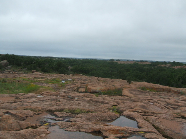 Rocky landscape with trees and puddles under a cloudy sky. Supermotors logo visible