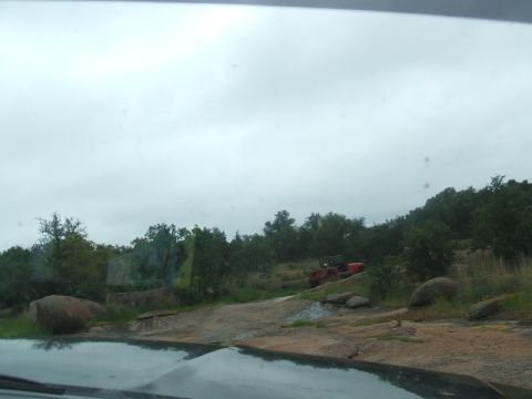 1995 Ford Bronco - A red off-road vehicle is parked on a rocky incline under a cloudy sky.