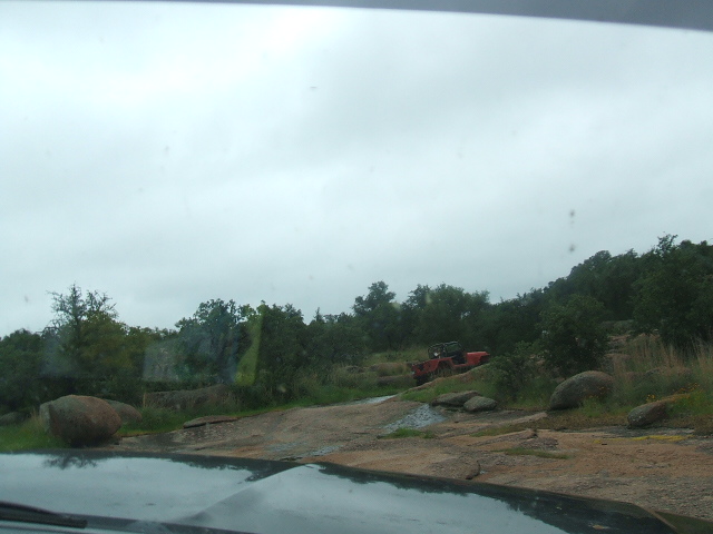 Red off-road vehicle parked on a rocky hill with trees in the background