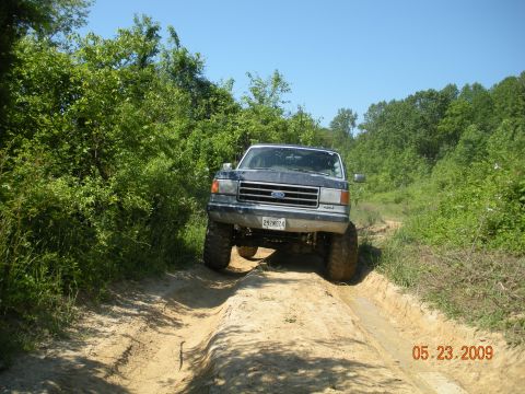 1998 Chevrolet Blazer - A lifted Ford truck navigates a muddy dirt track surrounded by dense foliage.