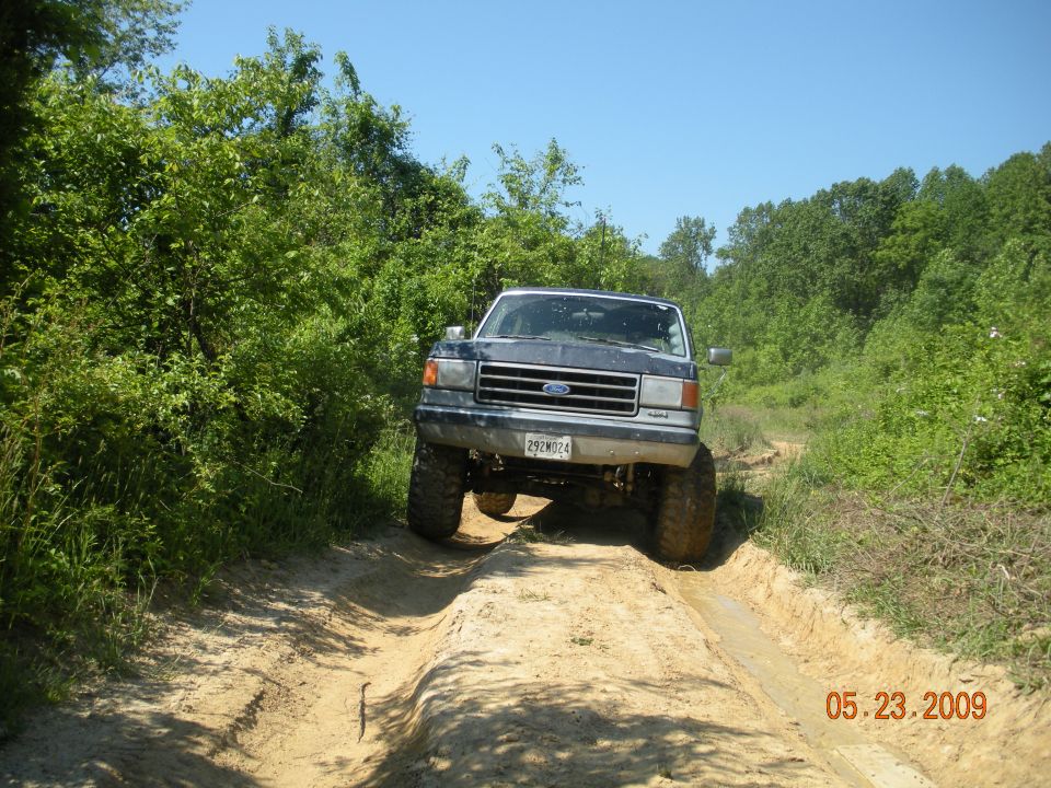 Dark gray Ford F-Series truck with lifted suspension driving on a dirt path