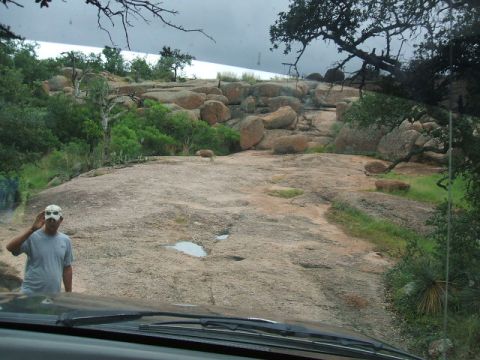 1995 Ford Bronco - A person in a mask stands on a rocky hill, viewed from inside a vehicle.