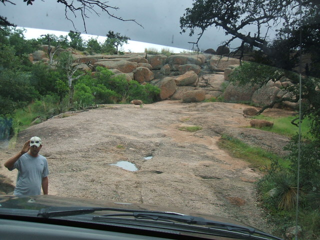 View from inside a vehicle looking out at a rocky landscape with a man wearing a mask