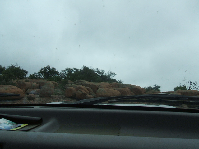 View from inside a vehicle looking out at a rocky landscape under a cloudy sky. The dashboard and windshield wipers are visible