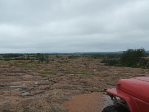 1995 Ford Bronco - Foreground shows part of a red vehicle against a backdrop of a rocky, arid landscape.