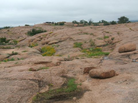 1995 Ford Bronco - A wide view of a rocky, arid landscape with several vehicles visible in the distance on a cloudy day.