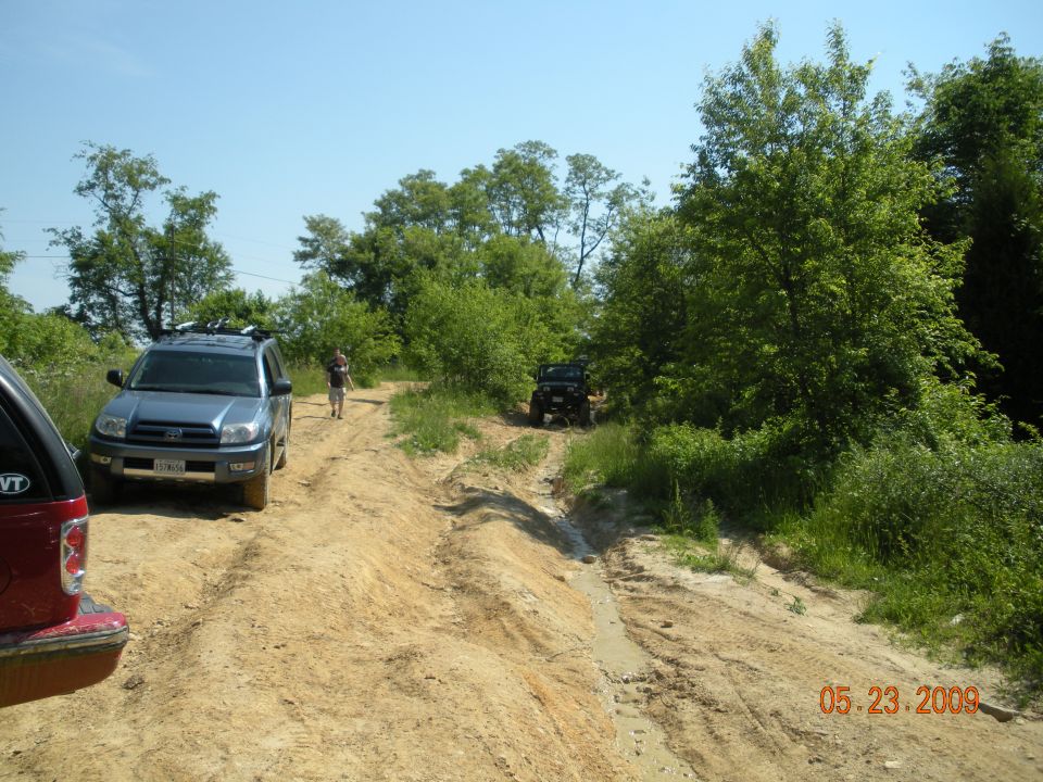 SUVs and a person on a sandy off-road trail lined with green trees