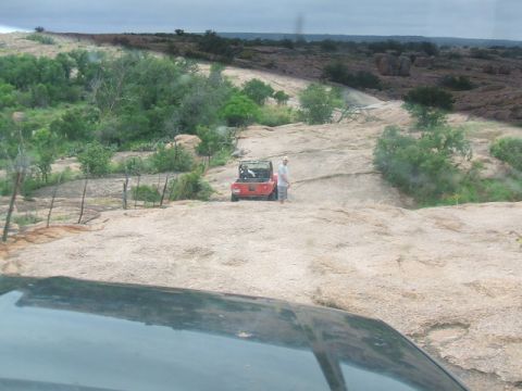 1995 Ford Bronco - A red Jeep Wrangler is parked on a rocky, off-road trail with a person standing beside it.