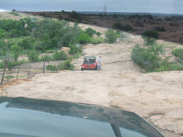 Red Jeep Wrangler on rocky landscape, person standing next to it