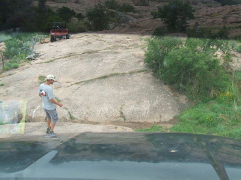 1995 Ford Bronco - A red off-road vehicle navigates a rocky landscape, viewed from the perspective of another vehicle.