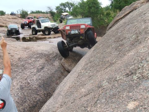 1995 Ford Bronco - Several off-road vehicles navigate a rocky terrain, with one Jeep Wrangler prominently climbing a large boulder.