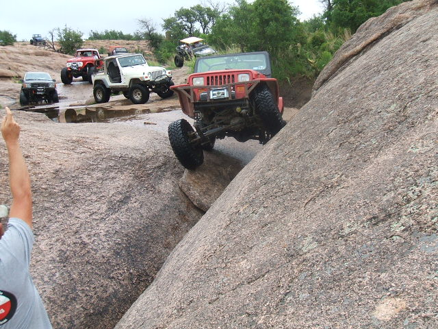 Red Jeep Wrangler climbing rocks with other off-road vehicles behind it