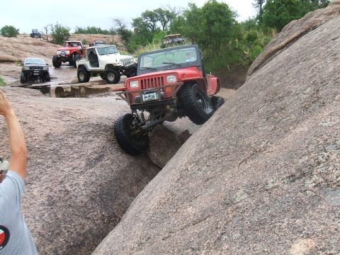 1995 Ford Bronco - Several off-road vehicles navigate a rocky terrain, with one Jeep prominently ascending a steep boulder.