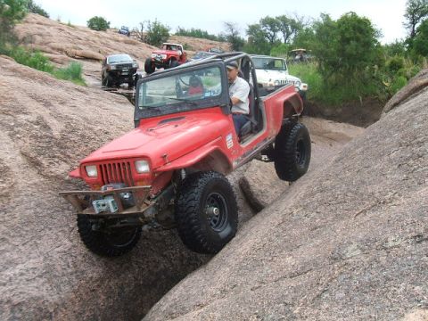1995 Ford Bronco - Off-road vehicles navigate a challenging rocky terrain, with a red Jeep Wrangler leading the way.