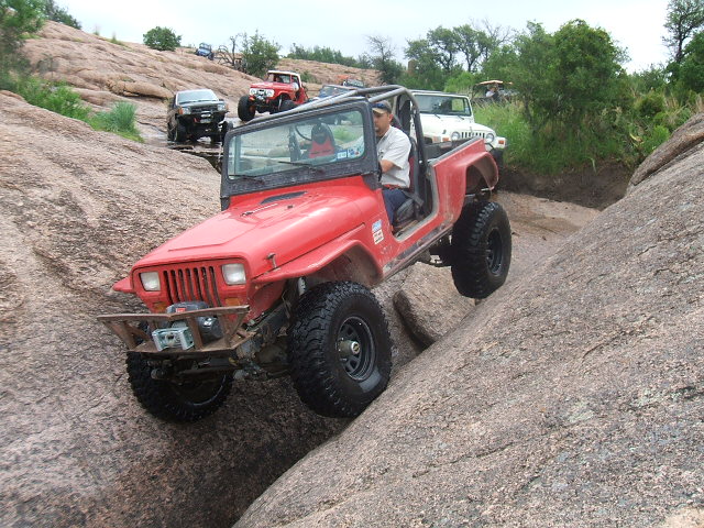 red Jeep Wrangler climbing a rocky hill with other off-road vehicles behind it