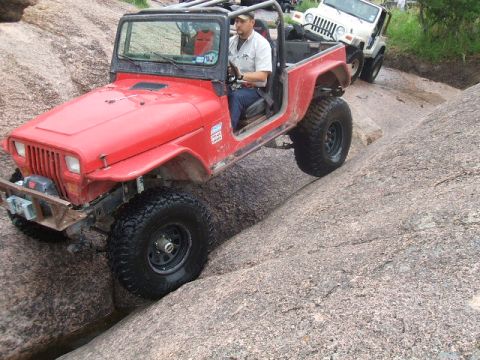 1995 Ford Bronco - A red Jeep Wrangler tackles a challenging rocky terrain, with another Jeep visible in the background.