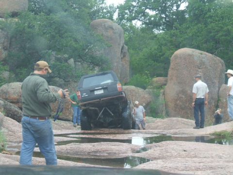 1995 Ford Bronco - A black Toyota SUV is shown off-roading over large rocks in a natural landscape.