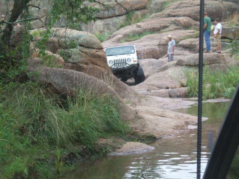 1995 Ford Bronco - A white Jeep navigates a rocky off-road trail with a stream running through it.