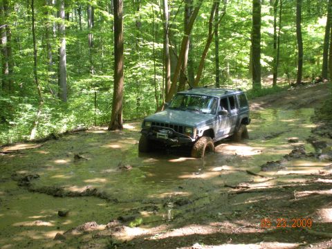 1998 Chevrolet Blazer - A Jeep Cherokee XJ navigates a muddy trail in a forest.