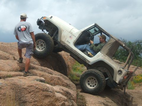 1995 Ford Bronco - A Jeep Wrangler navigates a challenging rocky terrain with a spotter nearby.