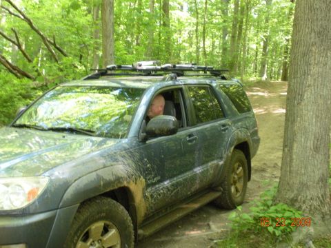 1998 Chevrolet Blazer - A dark green SUV with a roof rack navigates a muddy dirt road through a wooded area.