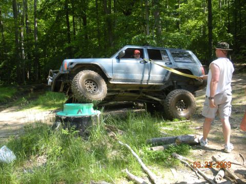 1998 Chevrolet Blazer - A lifted Jeep Cherokee XJ is being winched over a log obstacle on a wooded trail.