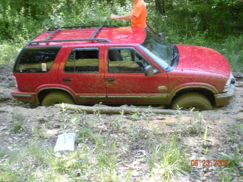 1998 Chevrolet Blazer - Red 1998 Chevrolet Blazer is stuck deep in mud with a person on its roof.
