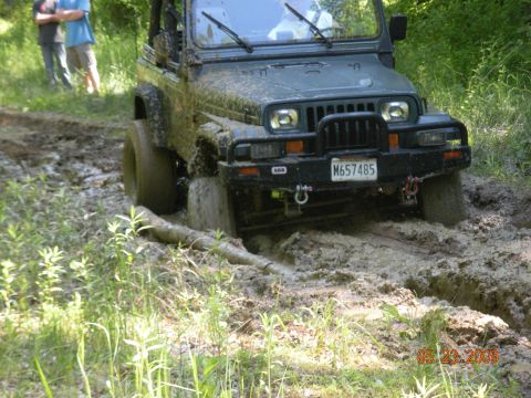 1998 Chevrolet Blazer - A Jeep Wrangler is stuck in deep mud on an off-road trail, with two onlookers in the background.