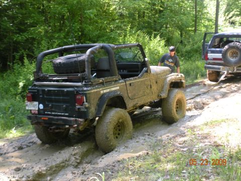 1998 Chevrolet Blazer - Two off-road vehicles navigate a muddy trail in a wooded area.
