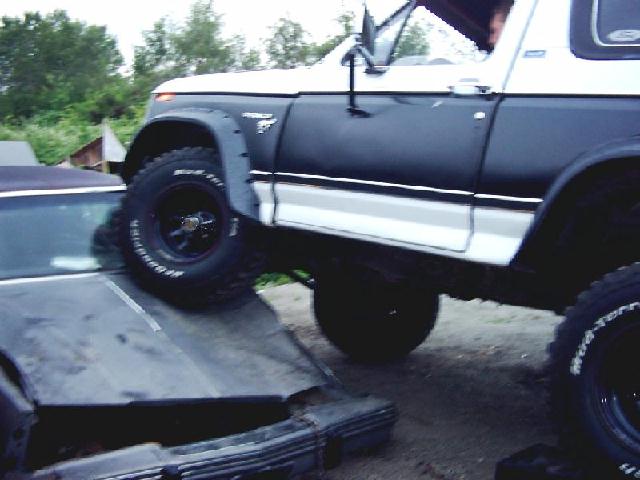 1980 Ford Bronco driving over a wrecked car's hood