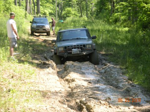 1998 Chevrolet Blazer - Two off-road vehicles navigate a muddy path through a wooded area.
