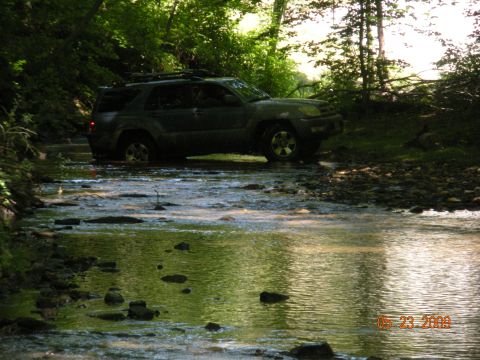 1998 Chevrolet Blazer - SUV navigates a rocky stream bed surrounded by dense forest on a sunny day.