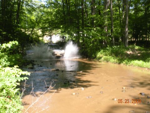 1998 Chevrolet Blazer - An SUV navigates through a muddy water crossing surrounded by trees.