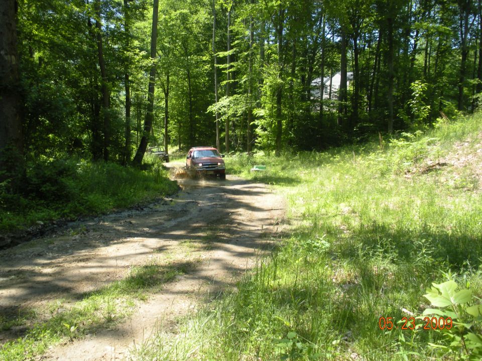 Red 1998 Chevrolet Blazer driving through a muddy path in a forest